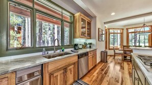 Une cuisine moderne avec des meubles en bois, un lave-vaisselle et une grande fenêtre donnant sur une forêt.