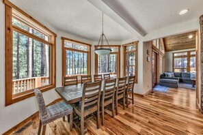A dining area with a wooden table and chairs, large windows with a view of trees, and a hanging light fixture. - Large Cabin, Golf Views, Bunk Room, Game Loft (Truckee)