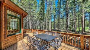 Une terrasse en bois avec une table et des chaises, entourée de grands arbres.