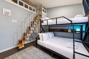 A bunk bed with white bedding, a wooden ladder, and a nightstand with a lamp.