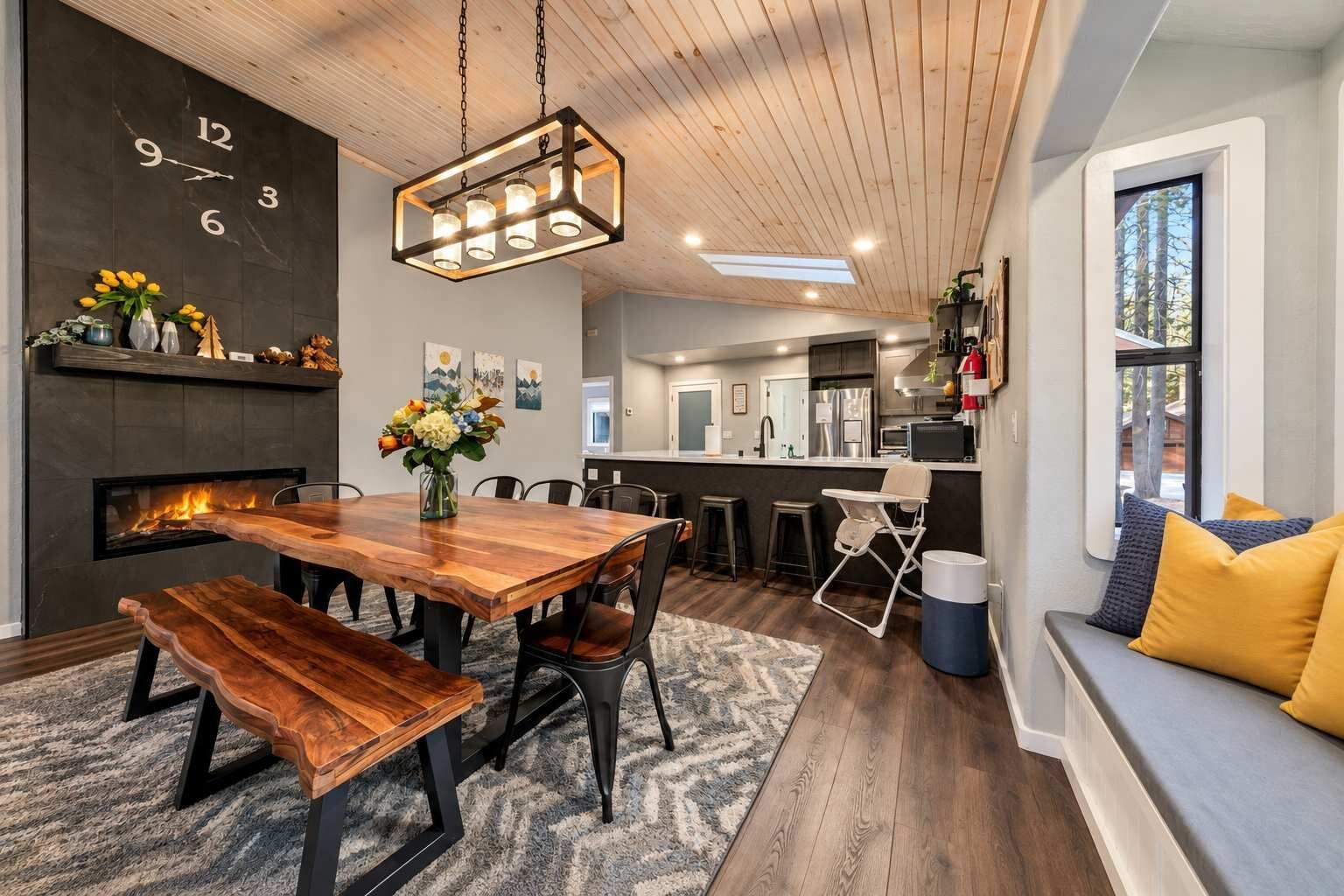 A modern kitchen with a central island, a dining area with a wooden table and benches, and a seating area with a bench and cushions.