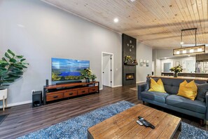 En moderne stue med et fladskærms-tv, et tv-møbel i træ, en sofa med gule puder og et sofabord.