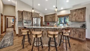 A modern kitchen with wooden cabinets, a central island with bar stools, stainless steel appliances, and pendant lighting. - New Tahoe Cabin with Hot Tub Games and EV Charger (South Lake Tahoe)