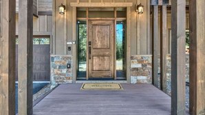 A wooden front door with a welcome mat, stone accents, and two wall-mounted lights. - New Tahoe Cabin with Hot Tub Games and EV Charger (South Lake Tahoe)
