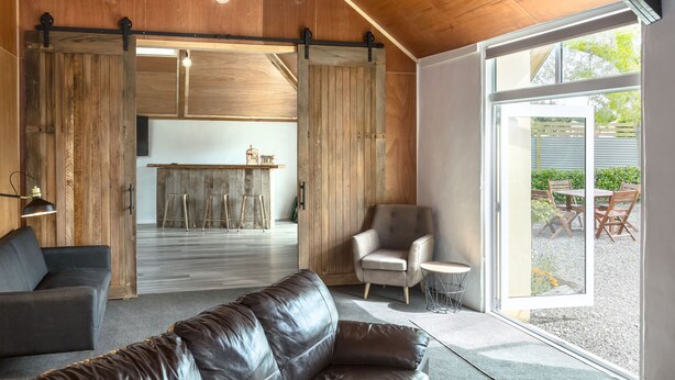 A modern interior with a leather sofa, a wooden dining area, and a sliding barn door. - Hidden Valley Getaway (Martinborough)