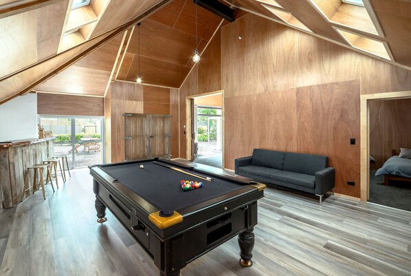 A spacious room with a pool table, wooden walls, and a sofa.