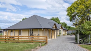 A building with a gravel driveway leading to a wooden fence and a gate. - Hidden Valley Getaway (Martinborough)