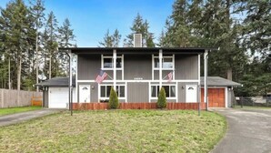 A two-story building with a garage, two American flags, and a small lawn in front. - Cozy 3 Bedroom Unit (Olympia)