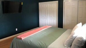 A bedroom with a bed, a television mounted on the wall, and two white doors. - Cozy 3 Bedroom Unit (Olympia)