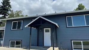 A two-story building with a dark exterior, a front door, and a small porch area. - New! Charming 4-Bedroom House (Des Moines)