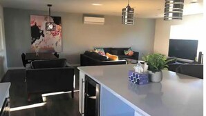 A modern living room with a grey sofa, a dining table, and a kitchen island. - New! Charming 4-Bedroom House (Des Moines)