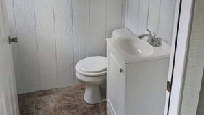 Une petite salle de bain aux murs recouverts de panneaux blancs, équipée de toilettes et d’un lavabo.