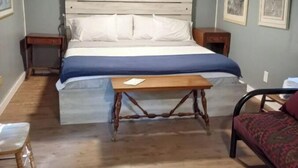 Une chambre à coucher comprenant un lit, des tables de chevet, une petite commode en bois, une petite table et une chaise.