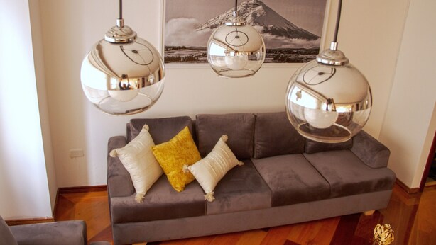 A modern living room with a gray sofa, three spherical pendant lights, and a framed picture of a mountain on the wall. - NICE APARTMENT, CLOSE TO EVERYTHING. (Quito)