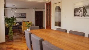 A dining area with a wooden table and grey upholstered chairs, a sofa, and a potted plant. - NICE APARTMENT, CLOSE TO EVERYTHING. (Quito)