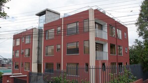 A modern multi-story building with a red facade, multiple balconies, and a gated entrance. - NICE APARTMENT, CLOSE TO EVERYTHING. (Quito)
