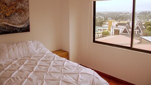 A bedroom with a large bed, a nightstand, a painting on the wall, and a window offering a city view. - NICE APARTMENT, CLOSE TO EVERYTHING. (Quito)