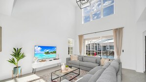 Un salon spacieux avec un grand canapé gris, une table basse et un téléviseur diffusant une scène de plage tropicale.