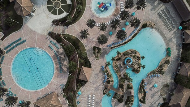 Vue aérienne d’un complexe hôtelier doté d’une grande piscine centrale, d’une plus petite piscine circulaire et d’un toboggan aquatique.