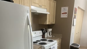 Une cuisine avec un réfrigérateur, une cuisinière et un four blancs, des armoires en bois, une machine à café et une poubelle.