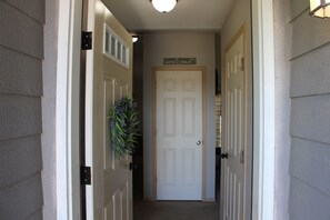 A hallway with a closed door, a welcome sign, and a plant on the left. - Baker Valley Home (North Powder)