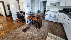 Une cuisine moderne avec des meubles blancs, une table à manger en bois avec des tabourets, un four à micro-ondes et une cuisinière.