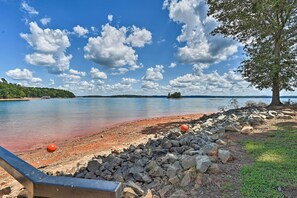Blick auf einen See mit steiniger Uferlinie, einem Baum und einer entfernten Insel.
