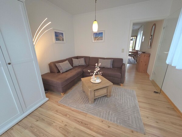 Un salon avec un canapé d’angle marron, une table basse en bois et un tapis. Deux tableaux encadrés sont accrochés au mur.