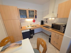 A compact kitchen with a dishwasher, microwave, sink, and wooden cabinets. - House Ekke Nekkepenn II, Whg. D1, close to the beach and the harbor - House Ekke (Wyk auf Föhr)