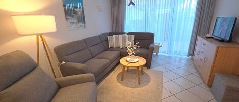 A modern living room with a sofa, armchair, coffee table, lamp, and a television on a cabinet.