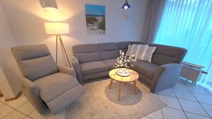 En moderne stue med en grå sofa, en grå lænestol, et rundt træsofabord og en gulvlampe.