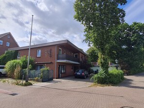 Ein zweistöckiges Gebäude mit Backsteinfassade und einem Balkon im oberen Geschoss. Vor dem Gebäude ist ein Auto geparkt.