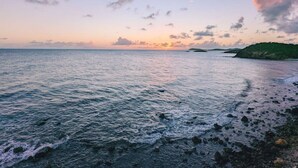 A coastal view with a calm sea, rocky shoreline, and a distant landmass. - "On the Rocks" Ocean Front 1BR/1BA Amazing Views! (St. Thomas)