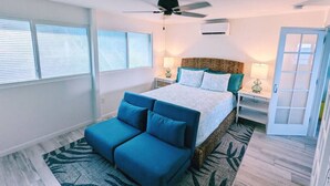 A bedroom with a bed, a ceiling fan, a nightstand, and a seating area. - "On the Rocks" Ocean Front 1BR/1BA Amazing Views! (St. Thomas)