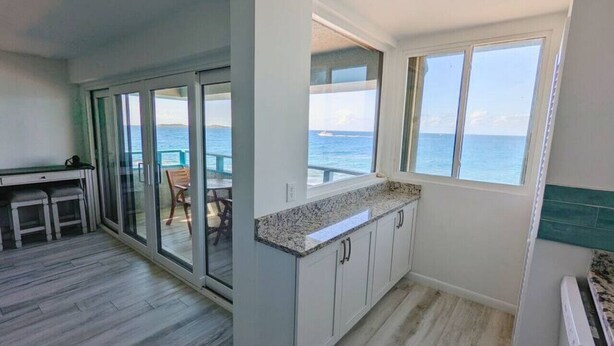 A kitchen with a view of the ocean, a dining area with a table and chairs, and a sliding glass door leading to an outdoor deck. - "On the Rocks" Ocean Front 1BR/1BA Amazing Views! (St. Thomas)