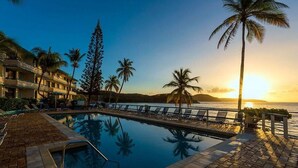 A poolside view with lounge chairs, palm trees, and a sunset. - "On the Rocks" Ocean Front 1BR/1BA Amazing Views! (St. Thomas)