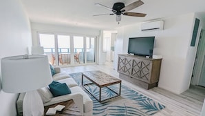 A modern living room with a sofa, coffee table, and a TV on a cabinet. - "On the Rocks" Ocean Front 1BR/1BA Amazing Views! (St. Thomas)