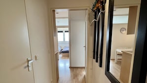 A narrow hallway with a wooden floor leading to a bedroom with a bed and a window.