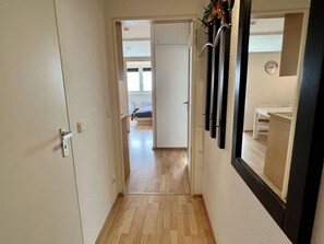 A narrow hallway with a wooden floor leading to a bedroom with a bed and a window.