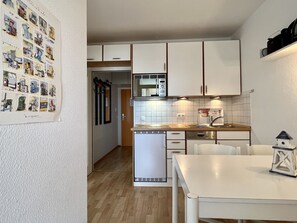 A compact kitchen with white cabinets, a microwave, and a dishwasher. There is a dining table with chairs and a small decorative item on the table.