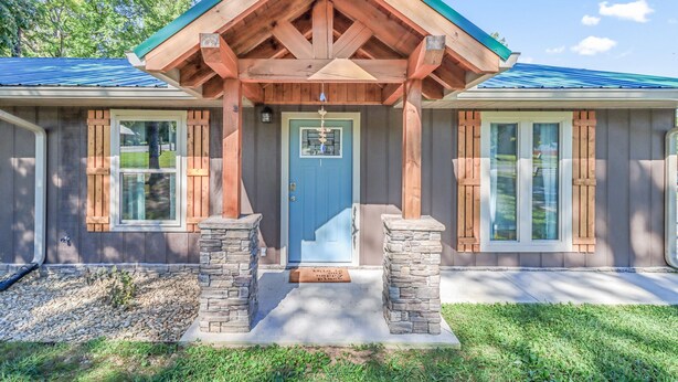 A wooden house with a blue door, stone pillars, and a covered porch. - Relaxing, family friendly lodge by the lake. (Ten Mile)