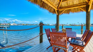 A wooden deck with a thatched roof, overlooking a body of water with a clear sky. - Intervillas Florida - Villa Manatee (Cape Coral)