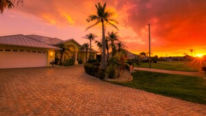 A residential driveway leading to a house with a garage, surrounded by palm trees and a well-maintained lawn. - Intervillas Florida - Villa Manatee (Cape Coral)