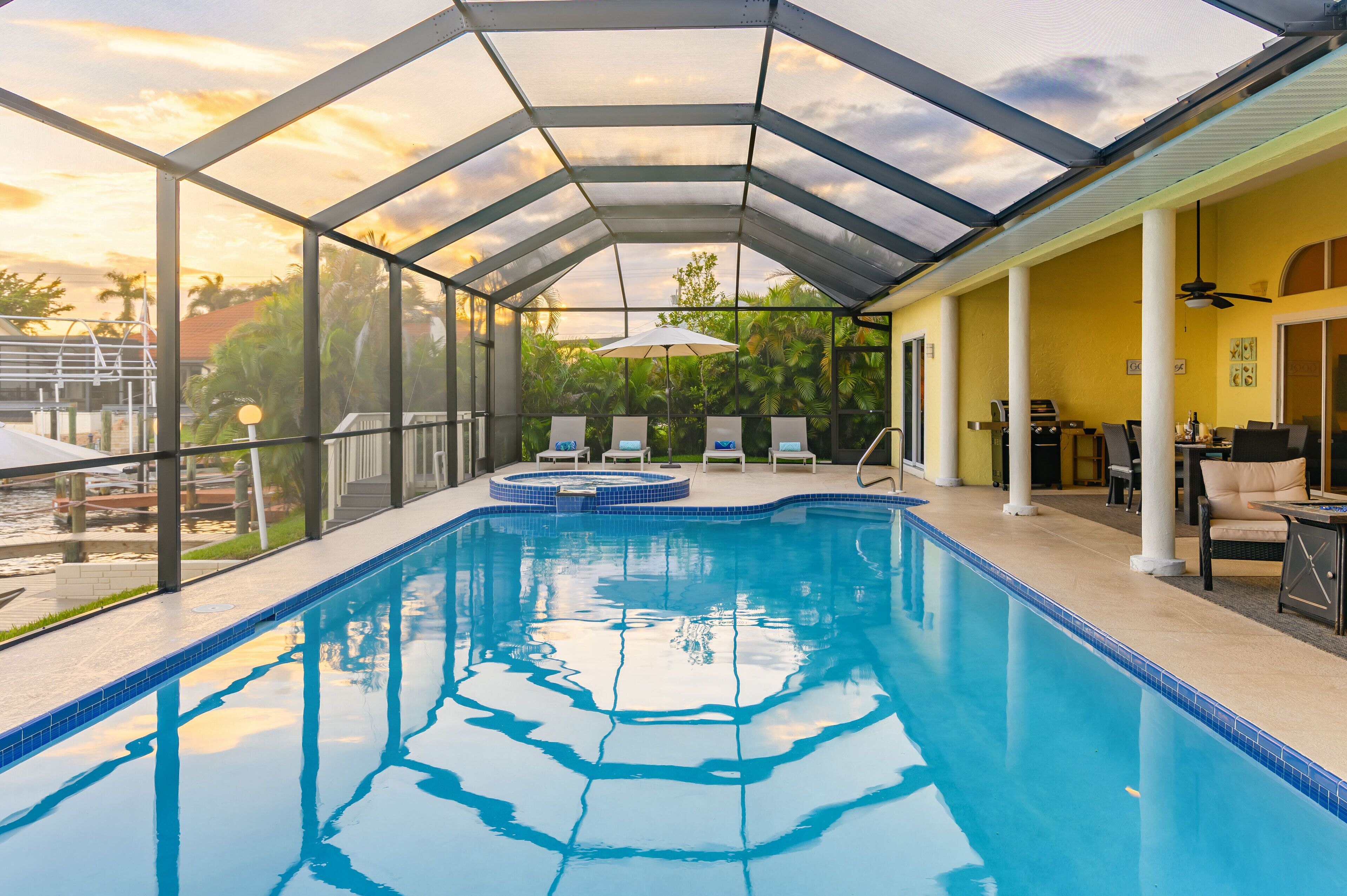 An indoor swimming pool with clear glass walls, a hot tub, and lounge chairs.