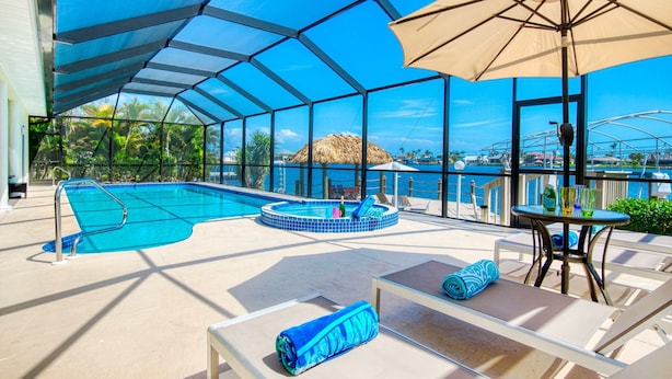 A pool area with a hot tub, lounge chairs, and umbrellas. - Intervillas Florida - Villa Manatee (Cape Coral)
