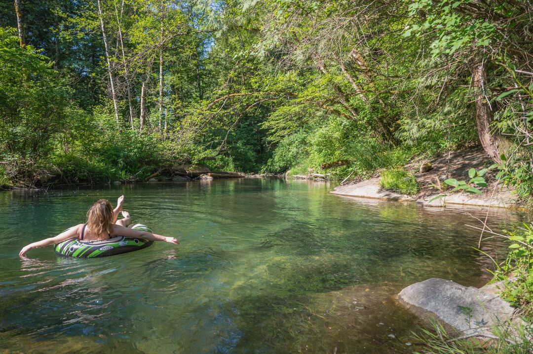A person floating on a tube in a clear river surrounded by dense greenery.