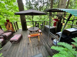 A wooden deck with outdoor furniture, including a bench and a table, surrounded by trees.