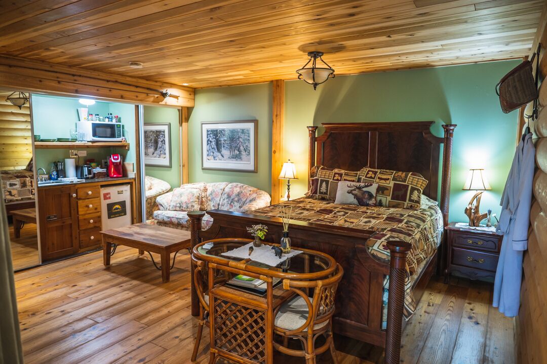 A cozy room with a wooden bed, a small desk, and a chair. There is a microwave and a coffee maker on the desk.