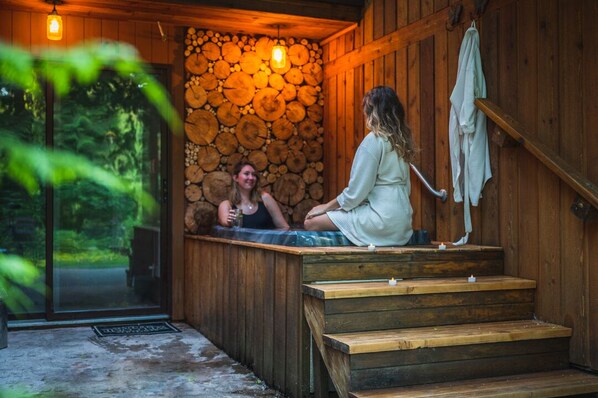 A wooden cabin with a hot tub, wooden steps, and a stone wall.