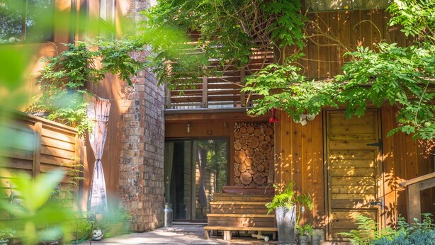 Un bâtiment en bois avec un mur en briques, une porte en bois et un escalier menant à une zone abritée.